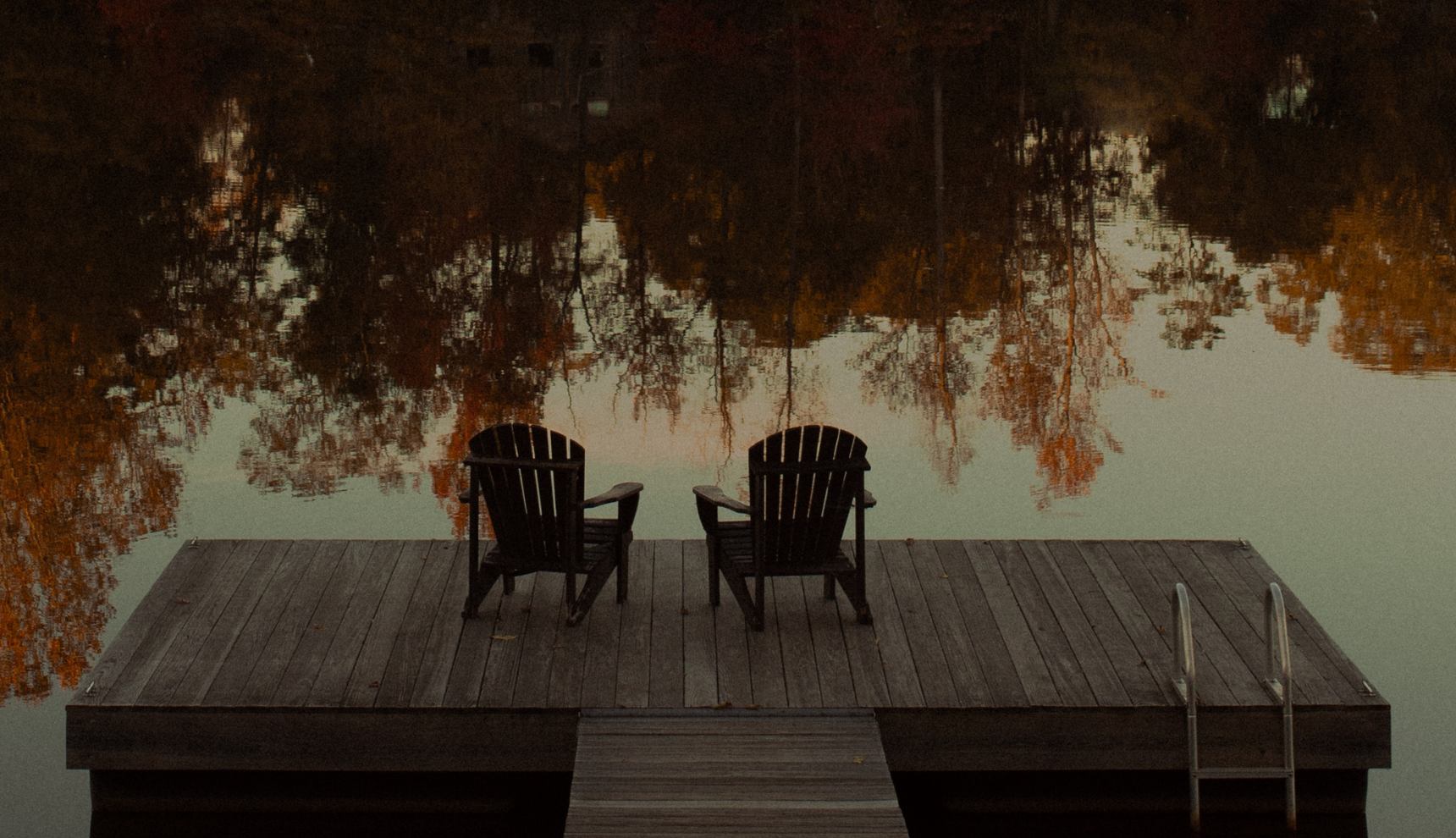 Two deck chairs on a wooden dock over a clear lake