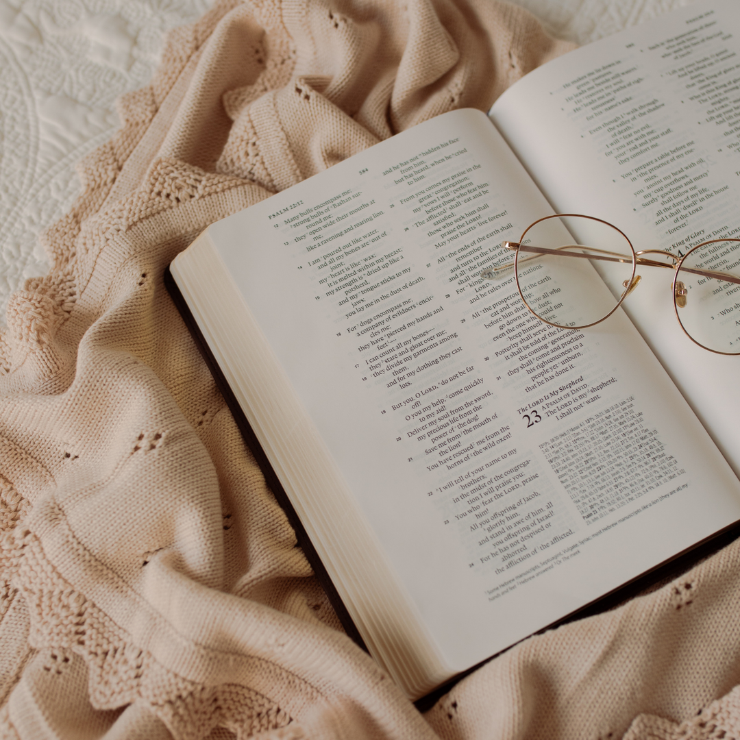 An Open Bible on a creme colored blanket with a pair of glasses on the pages