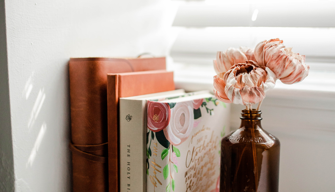 Some bible studies next to a windowsill and near a vase with some pink flowers in them