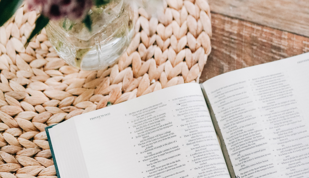 An open bible on a wooden table and a coral covered placemat