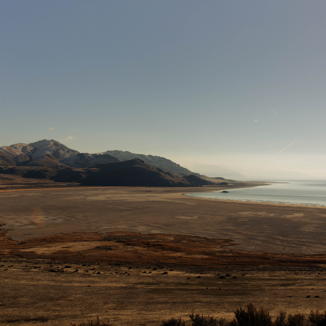 A field of sand and dirt near a mountain range and a lake