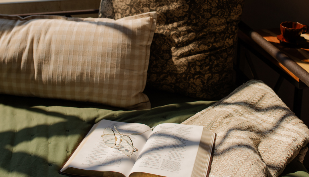 An open bible on a green bed spread near two pillows