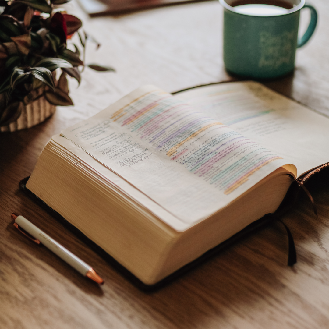 An open bible that has highlighted sections in it near a coffee cup and a pen