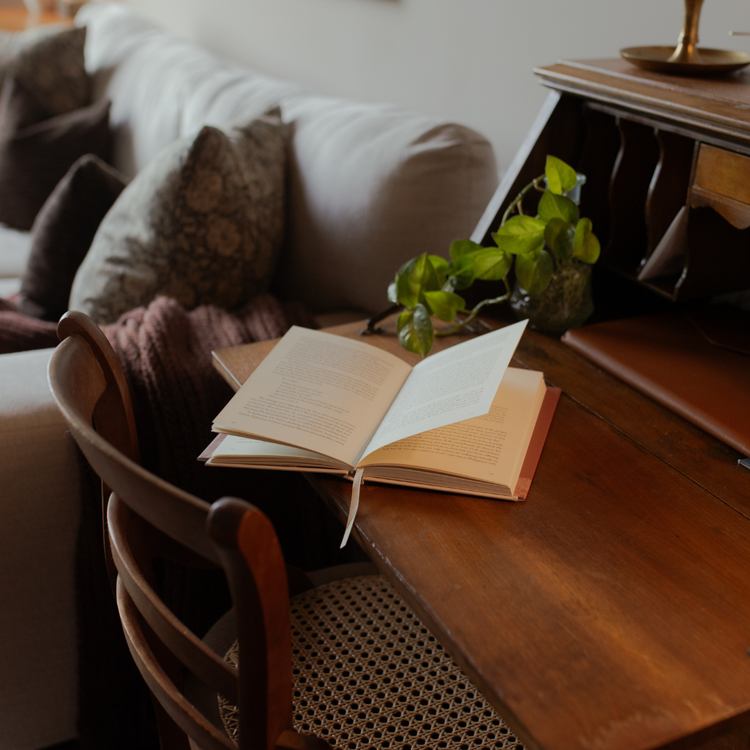 An open book on a wooden table near a woven chair