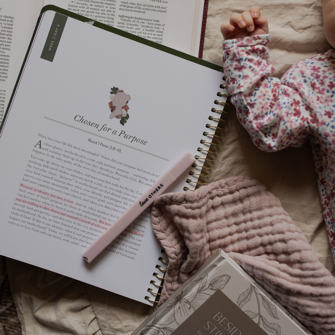 The Flourishing in motherhood opened on a blanket with a babies hand on the side with a highlighter resting on the page