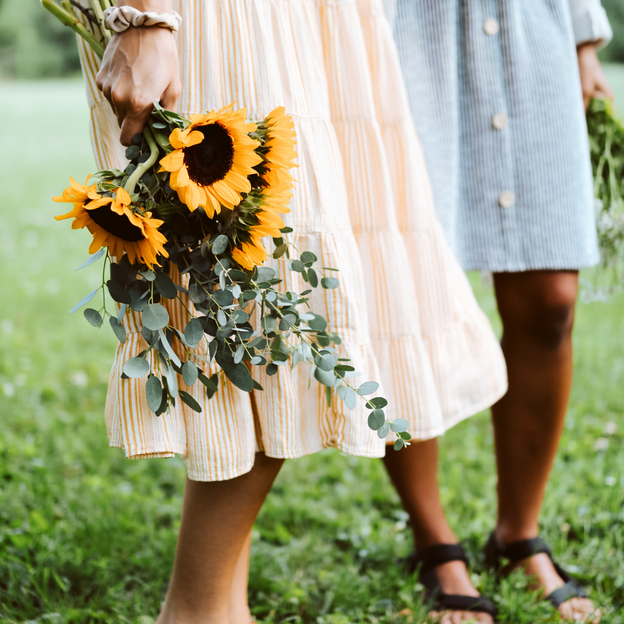 Two women in the grass with one of the women holding sunflowers