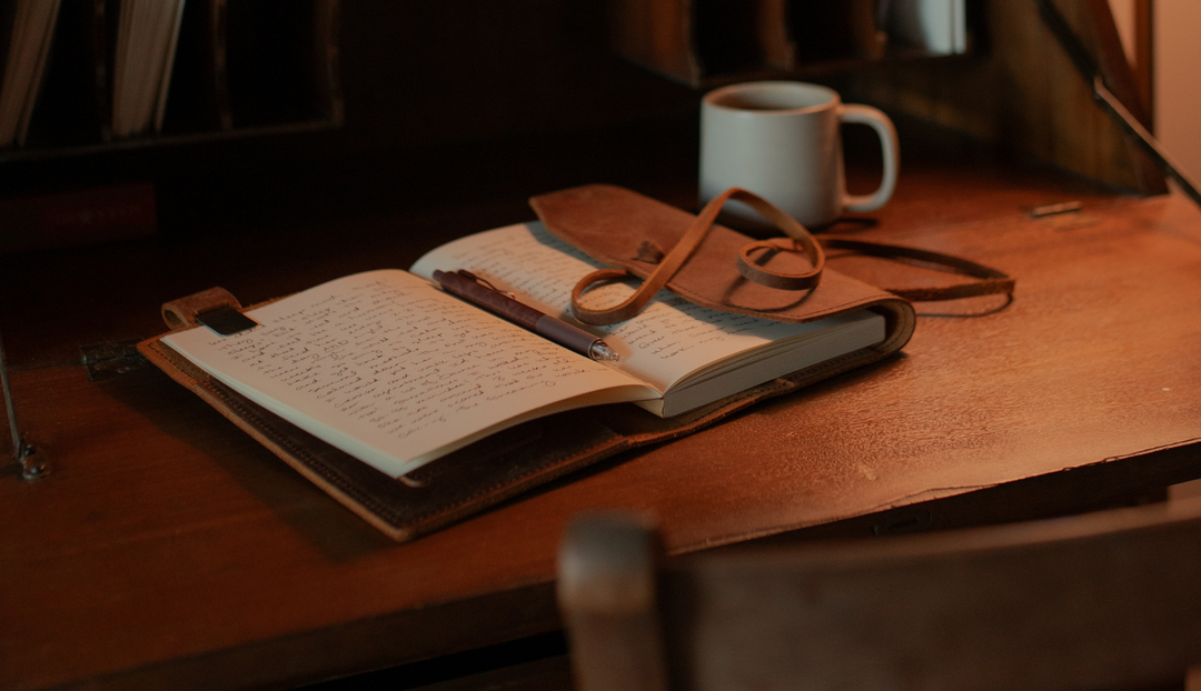 A leather wrapped bible opened on a wooden table near a coffee cup