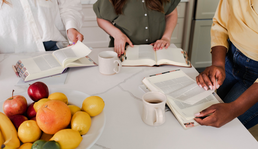3 women reading from an open bible on a white table