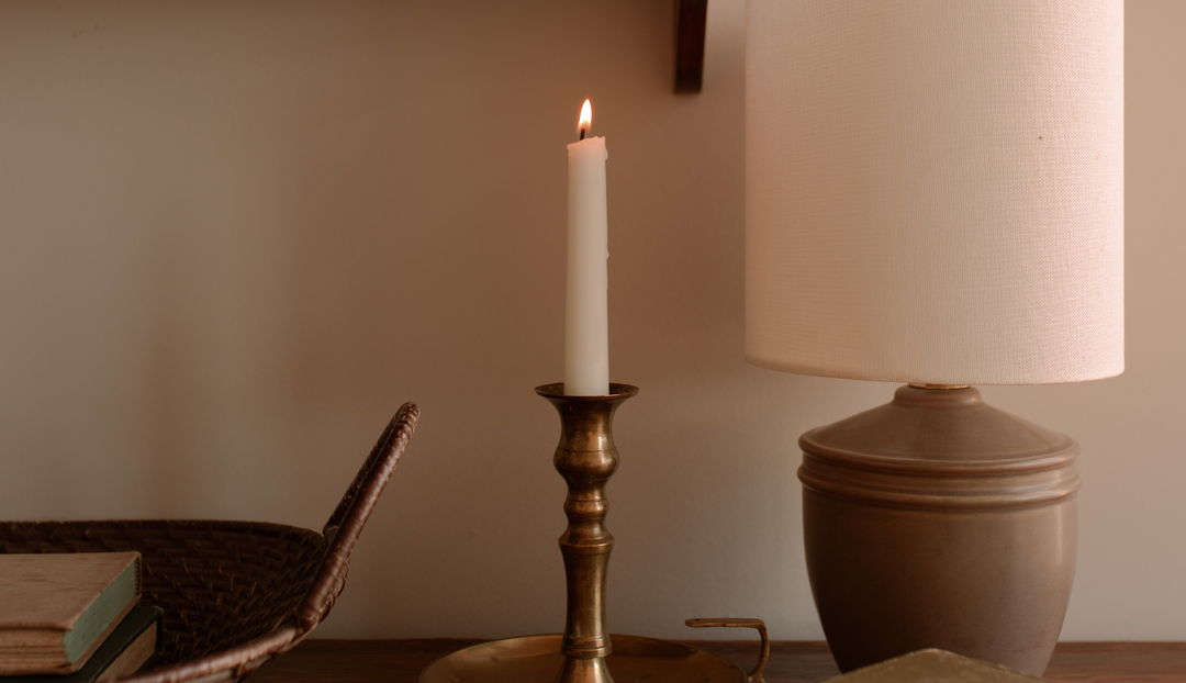 A lit candle near a lamp and a wicker basket