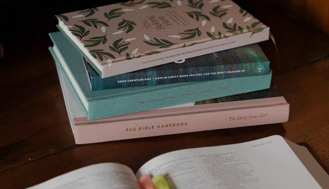 A stack of daily grace hardcover studies on a wooden table near an open bible