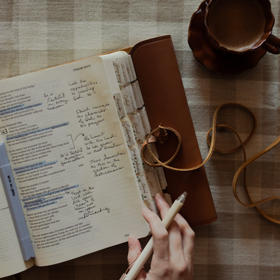 A woman's hand holding a pen near an open bible