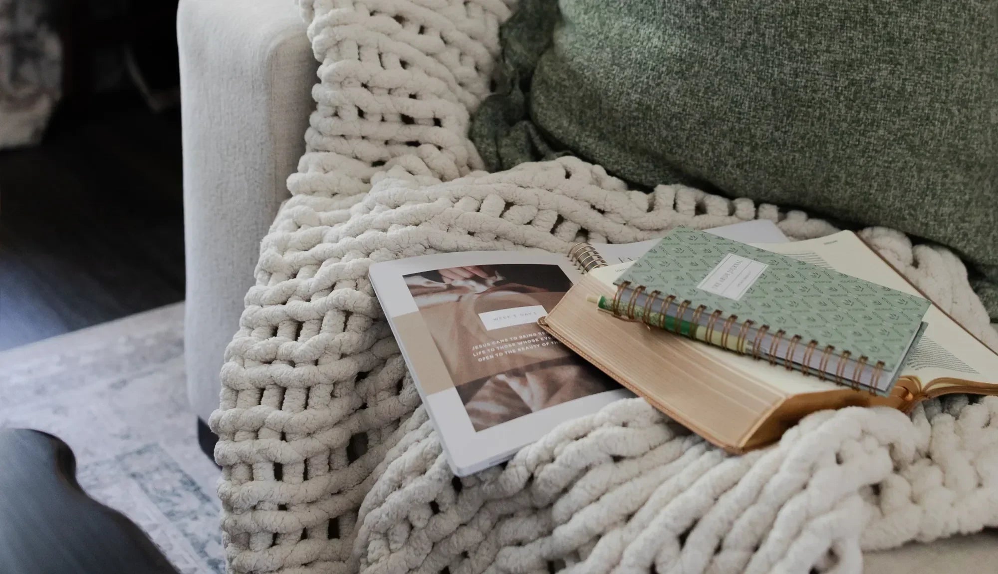 Multiple Daily Grace Bible studies and an open bible on a wavy knitted blanket on a couch