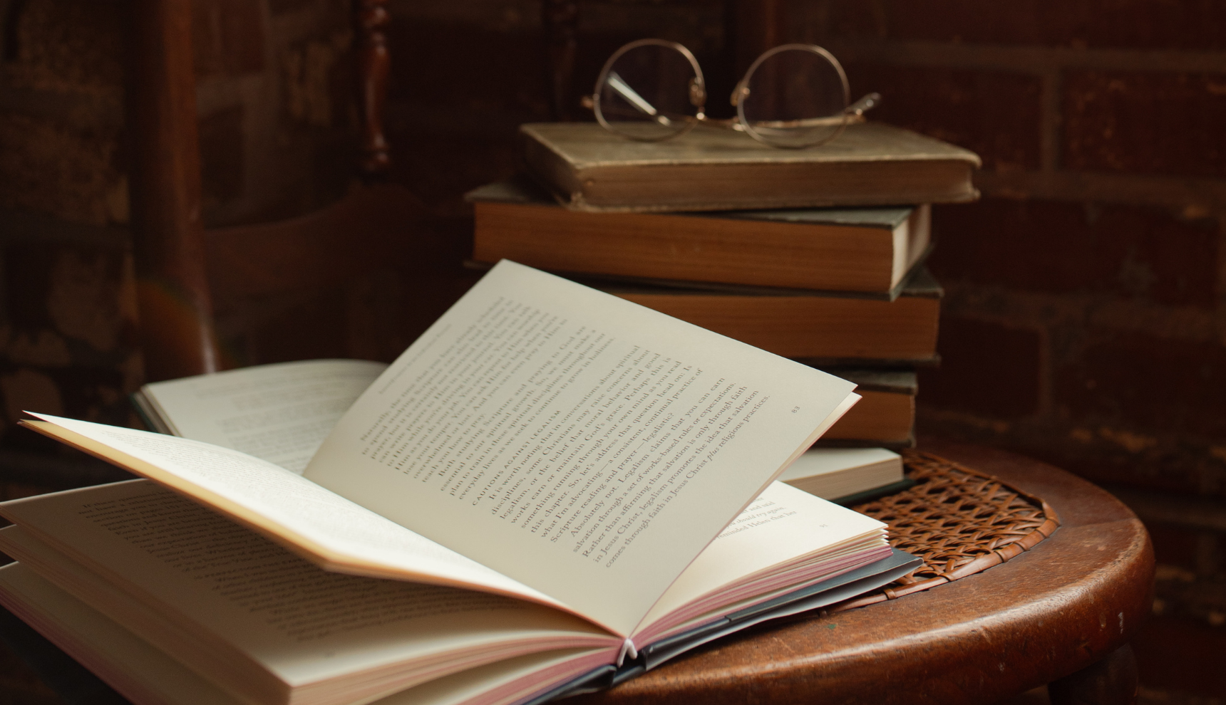 An open book with a stack of old books next to it on a wicker chair