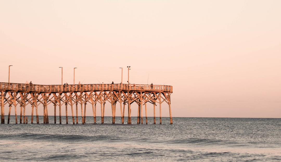 A pier overlooking a calm ocean with a rose colored sky