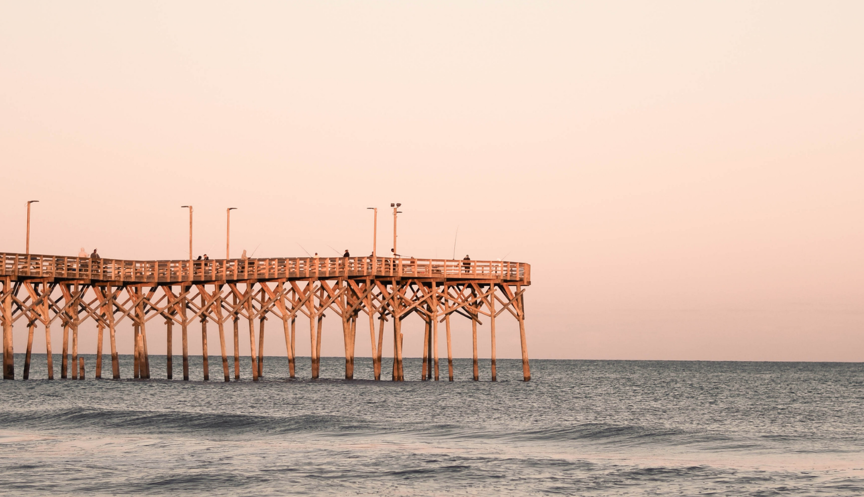A pier overlooking a calm ocean with a rose colored sky