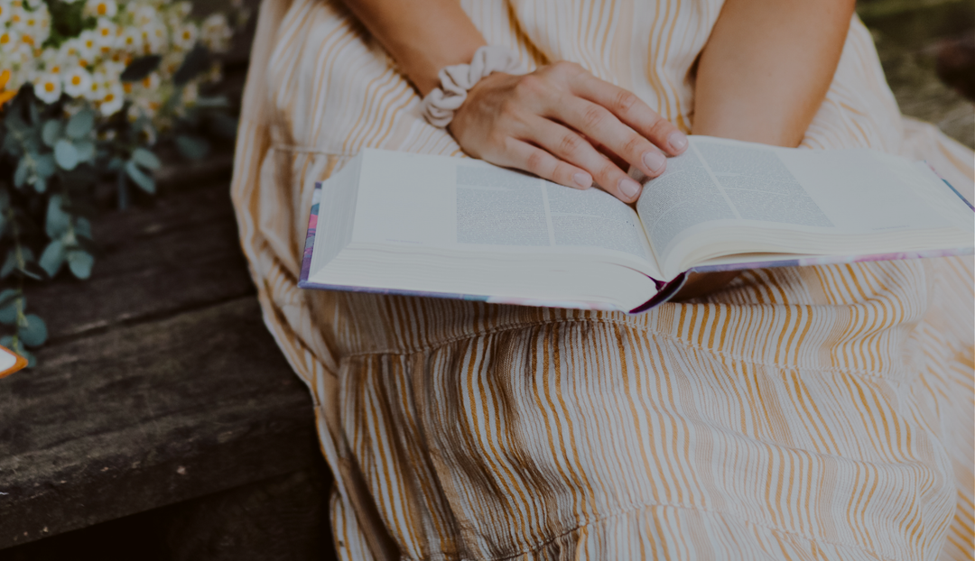 A woman reading from an open bible on a wooden bench