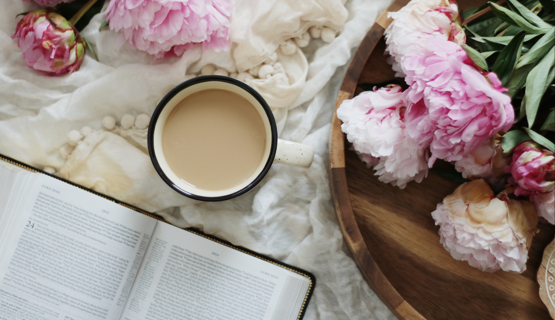 A coffee cup and an open bible near a wooden tray of fresh flowers