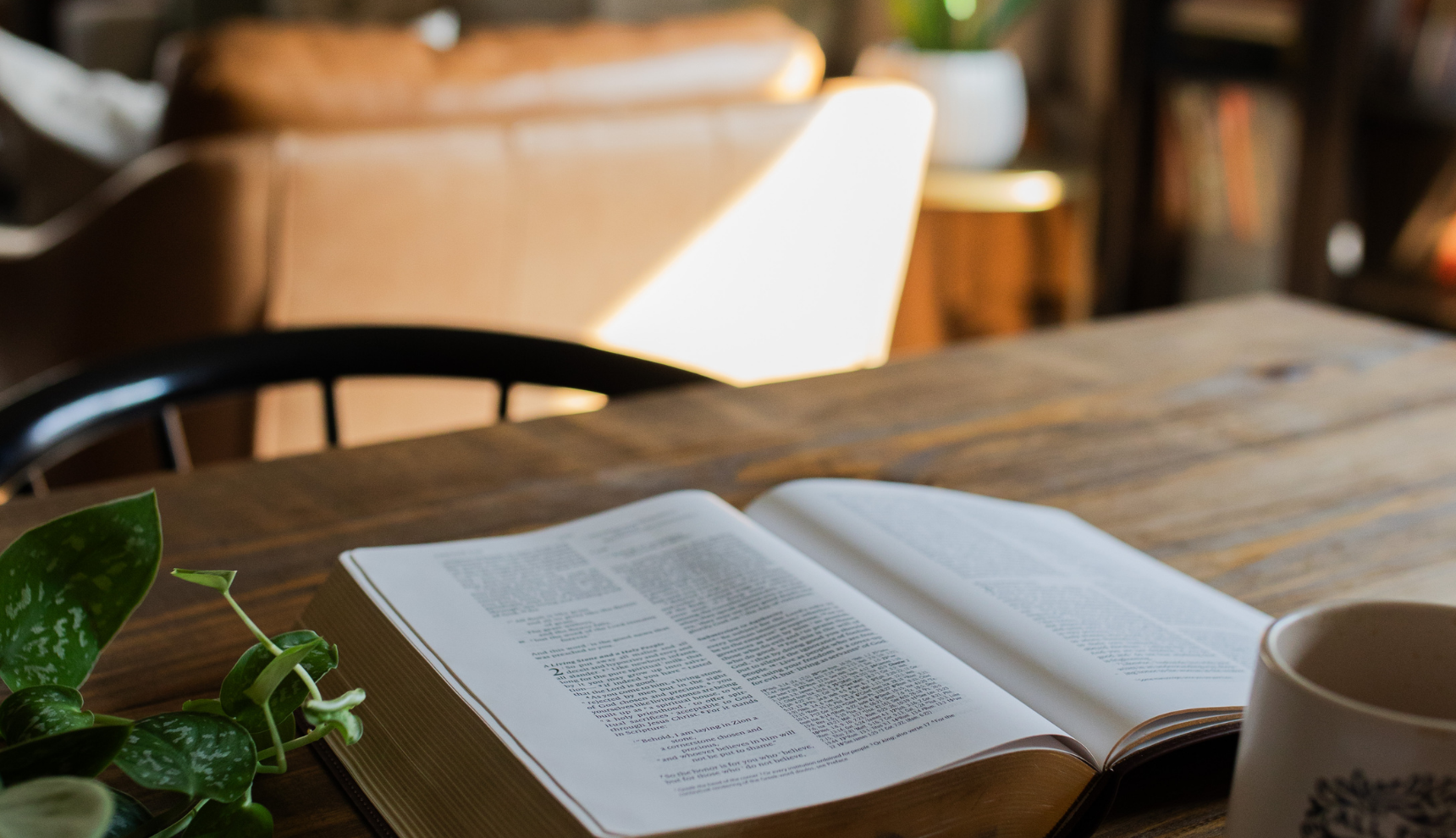 An open bible on a wooden table near a coffee cup