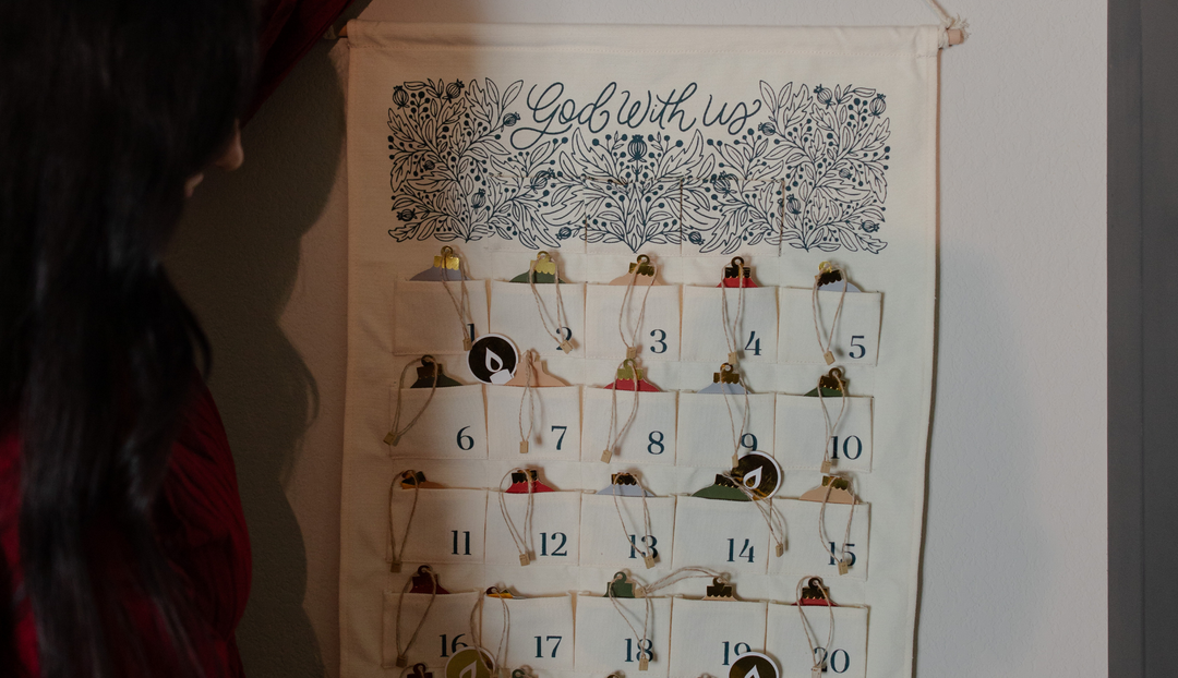 A woman hanging the Advent Wall calendar on a wall with advent ornaments on it