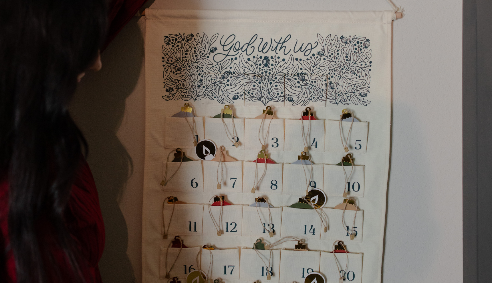 A woman hanging the Advent Wall calendar on a wall with advent ornaments on it