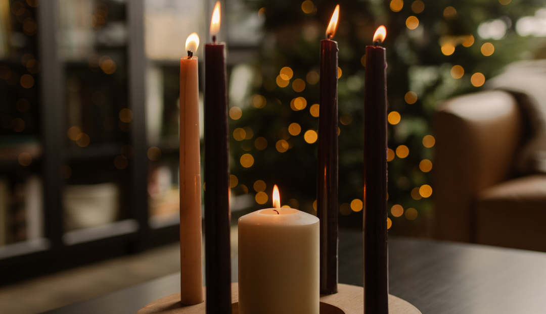 Multiple Advent candles lit on a wooden table with a tree in the background