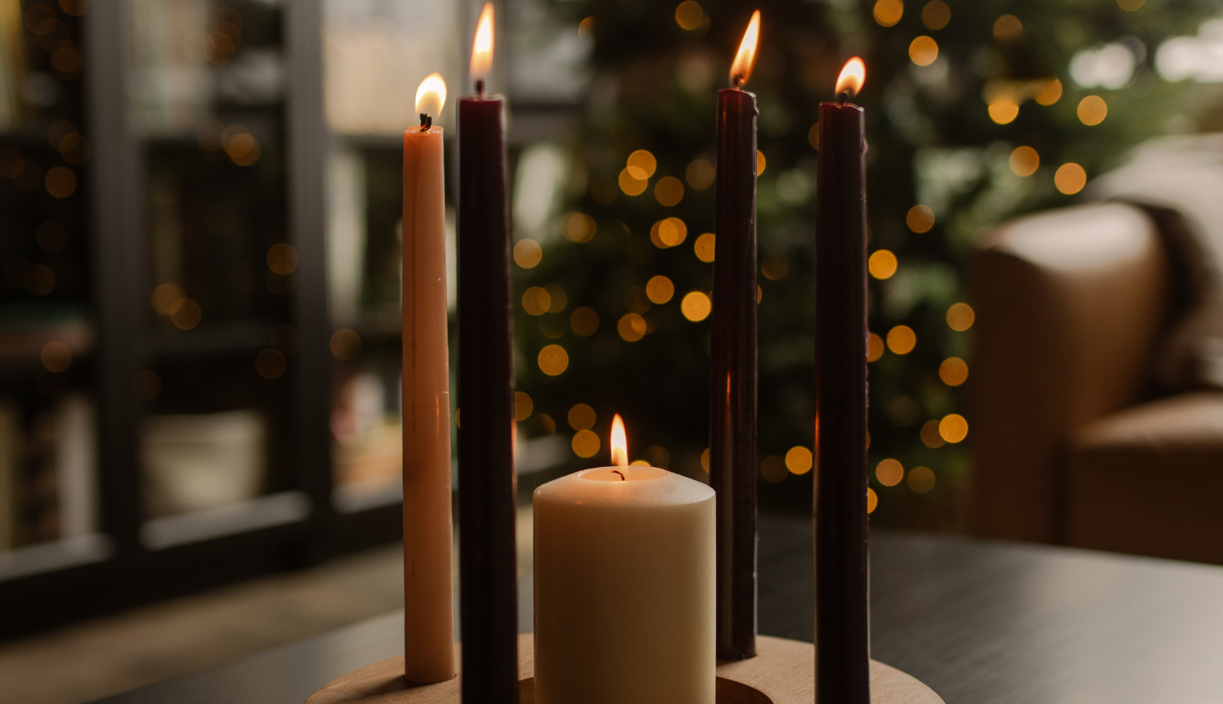 Multiple Advent candles lit on a wooden table with a tree in the background