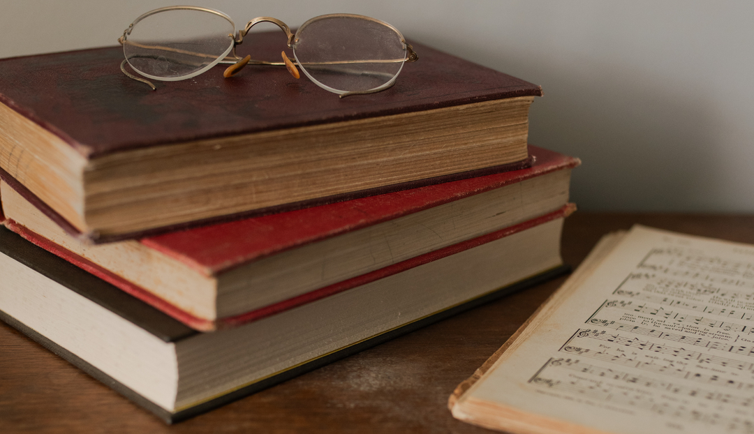 Multiple books stacked on a desk with a pair of glasses ontop