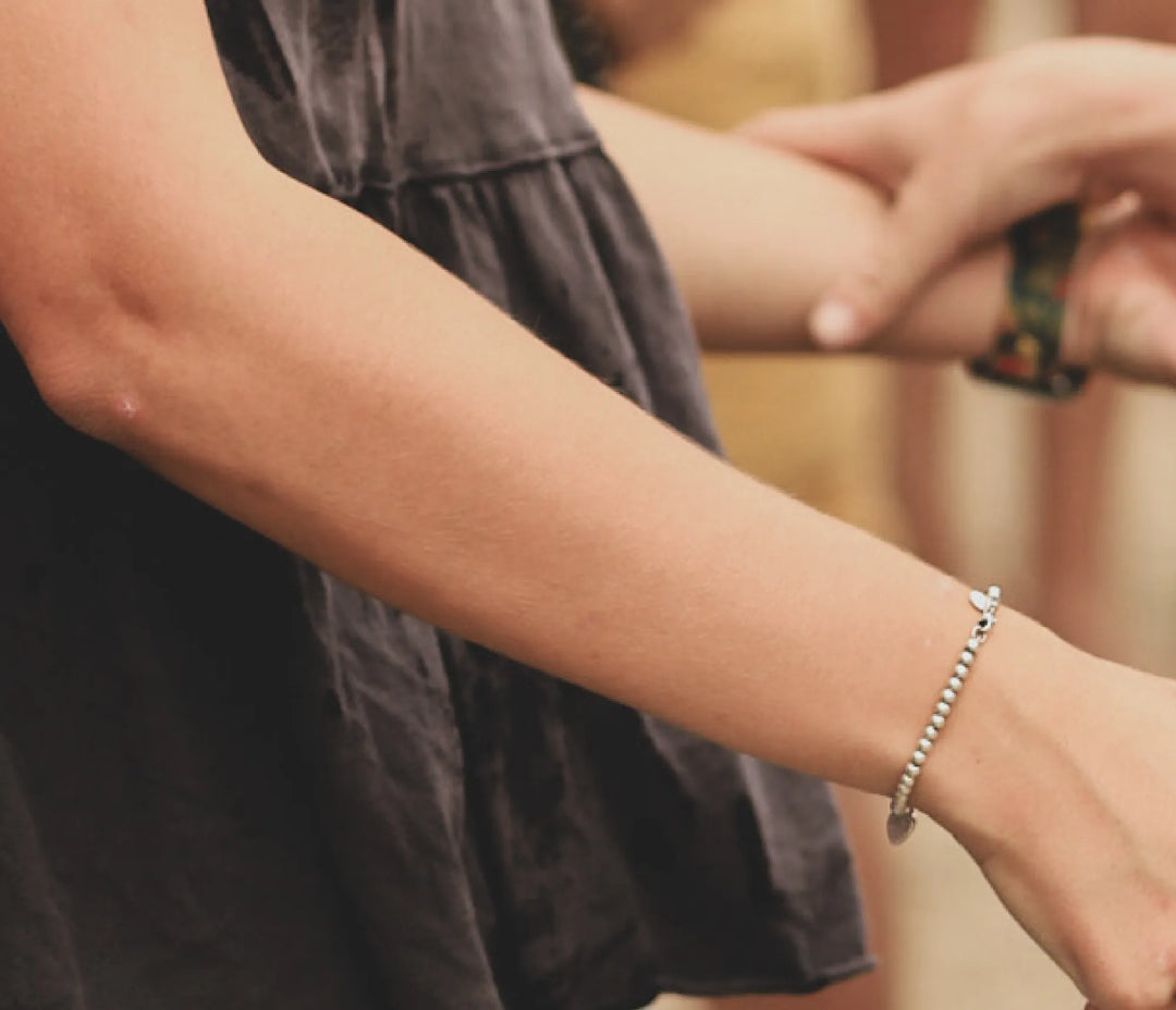 A close up of a woman's arm with a silver bracelet; The woman is wearing a black shirt