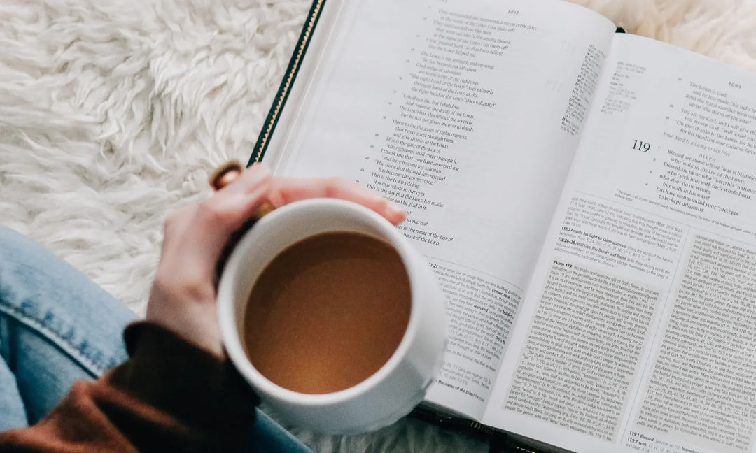 woman holding a white coffee cup over an open bible on the floor