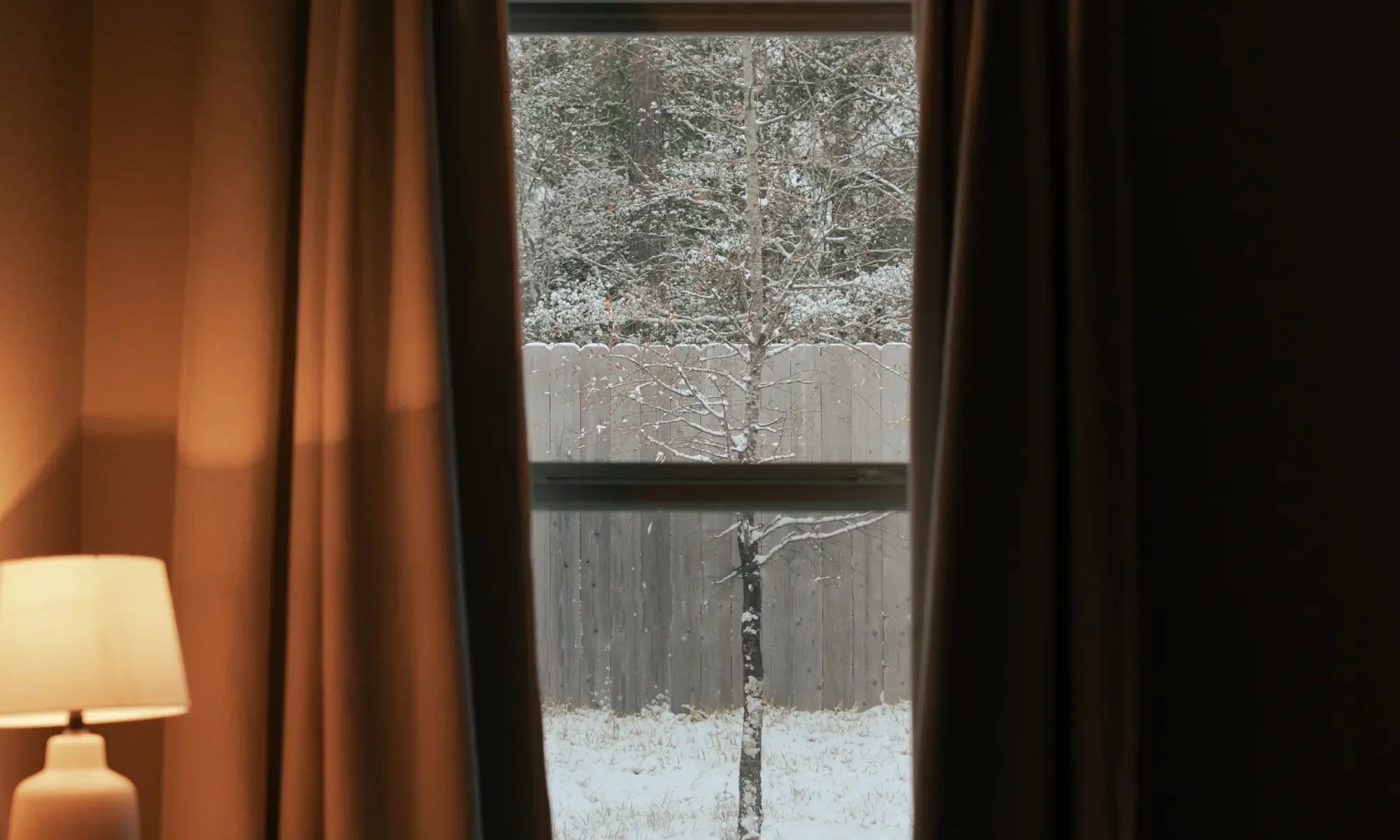 brown colored curtains next to a window showing it snowing outdoors