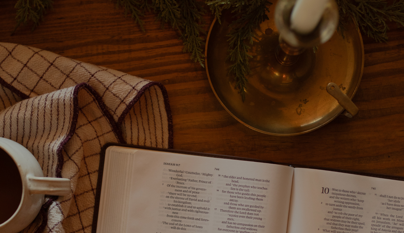 An open bible on a wooden table near a dishcloth and an bronze candle lamp