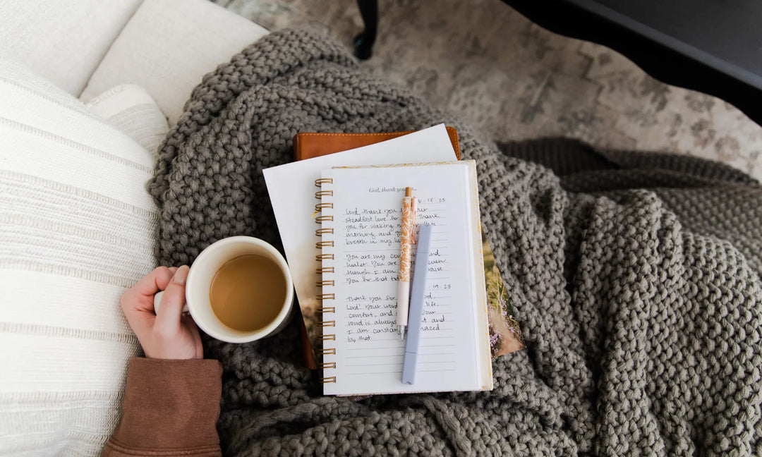 Journal open with pens laying on the page and a woman's hand holding a coffee cup