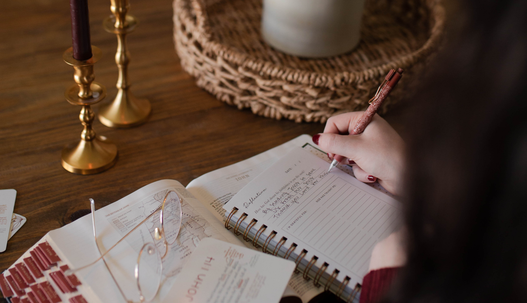 A woman writing in a journal with a pair of glasses on an open bible