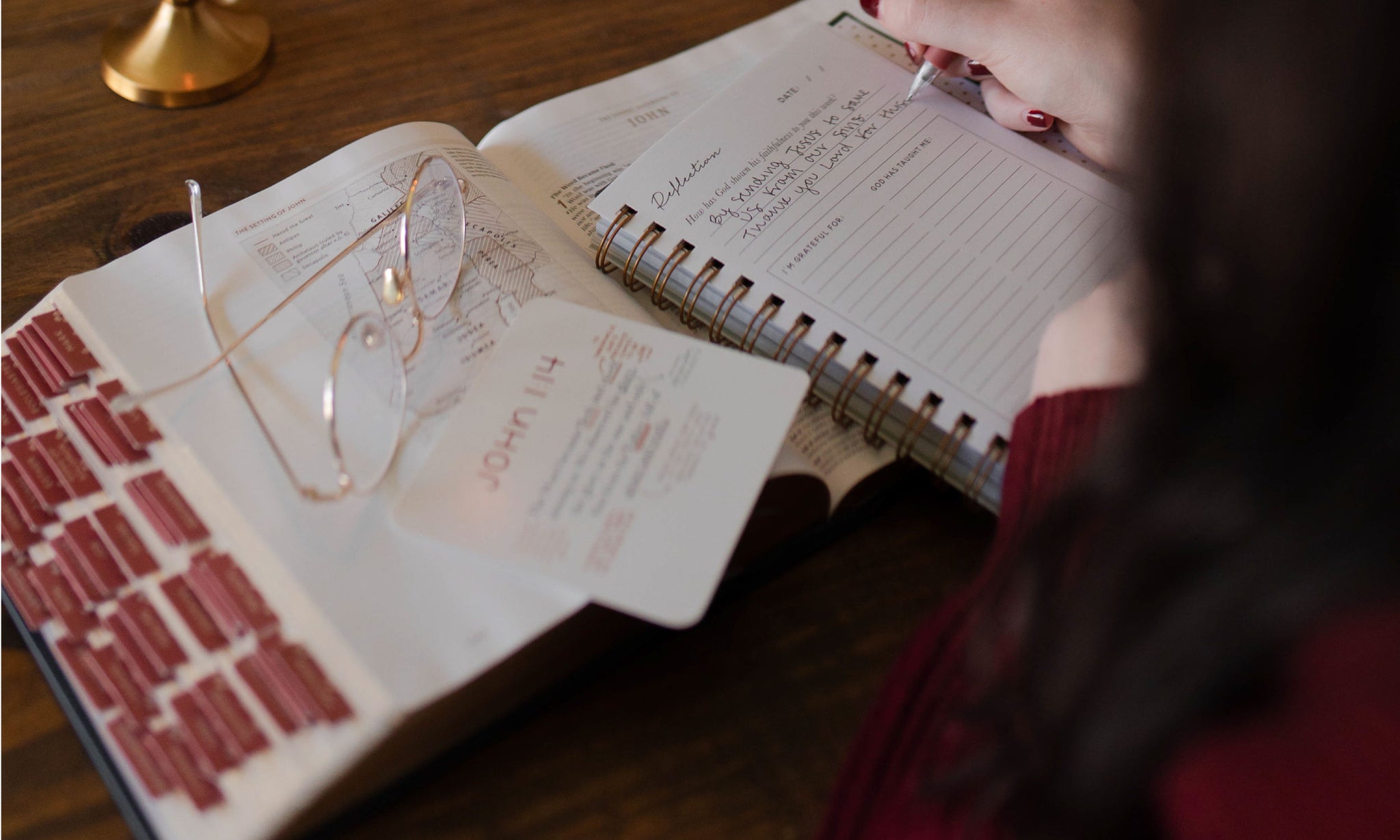 A woman writing in a notepad while a bible is open on the same table