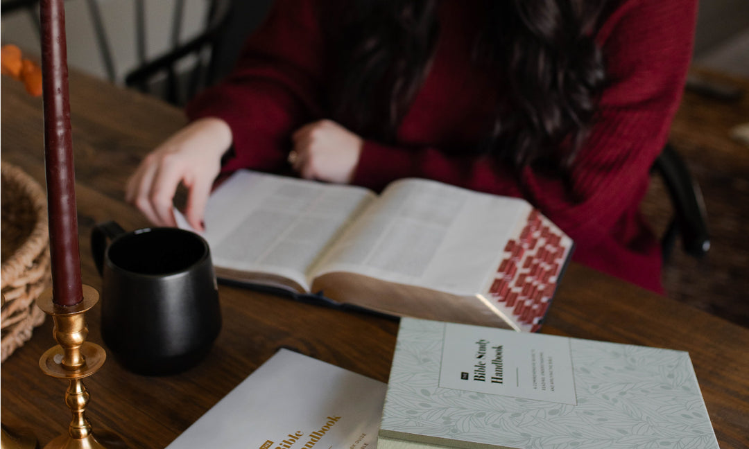 Someone sitting down reading their Bible at the table with a black coffee mug on the table.