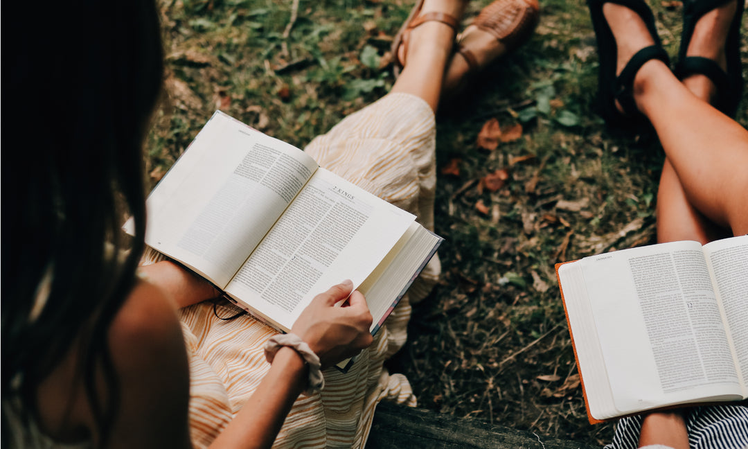 2 women sitting on the grass and reading their Bibles