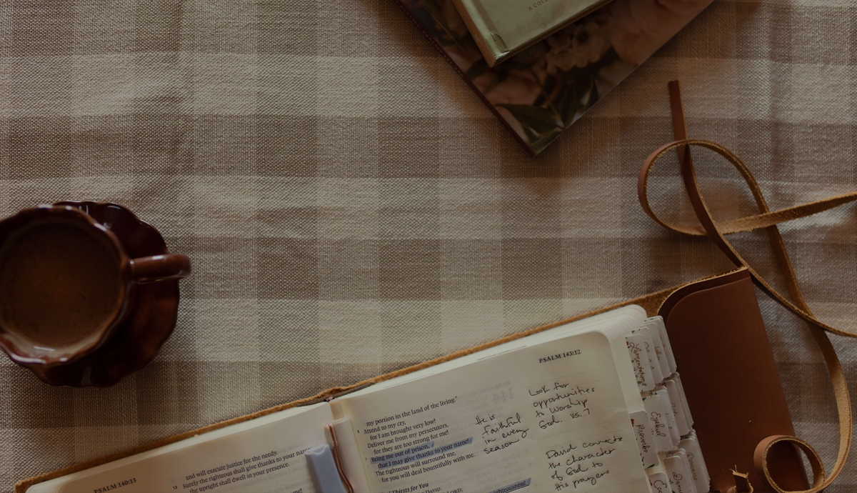 An open bible on a patterned tablecloth with a coffee cup on it
