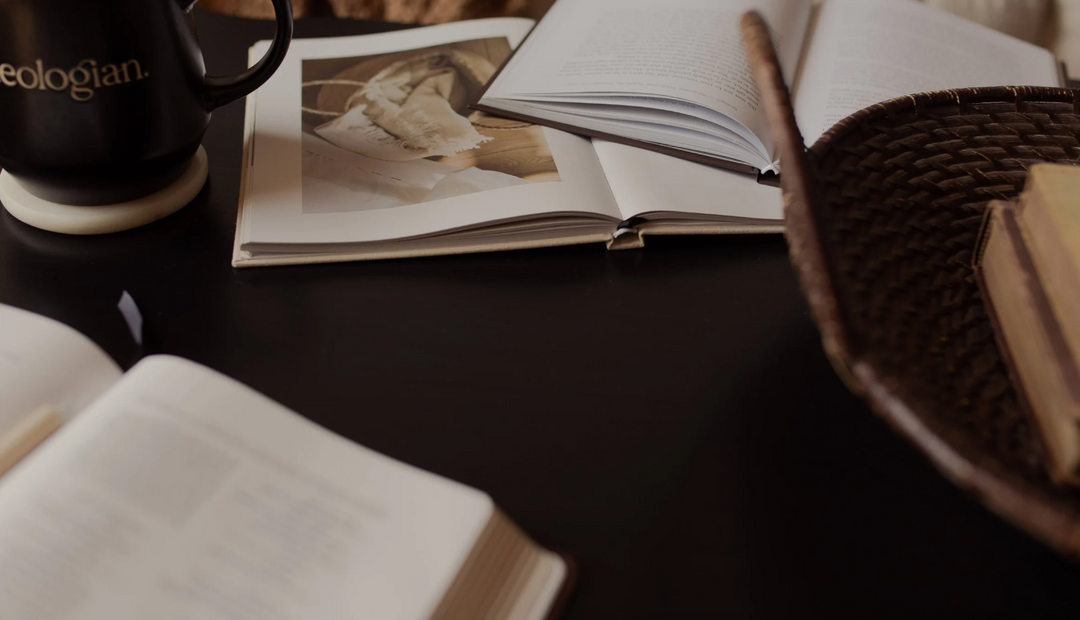 An open book on a dark colored table near a wicker basket and a coffee cup