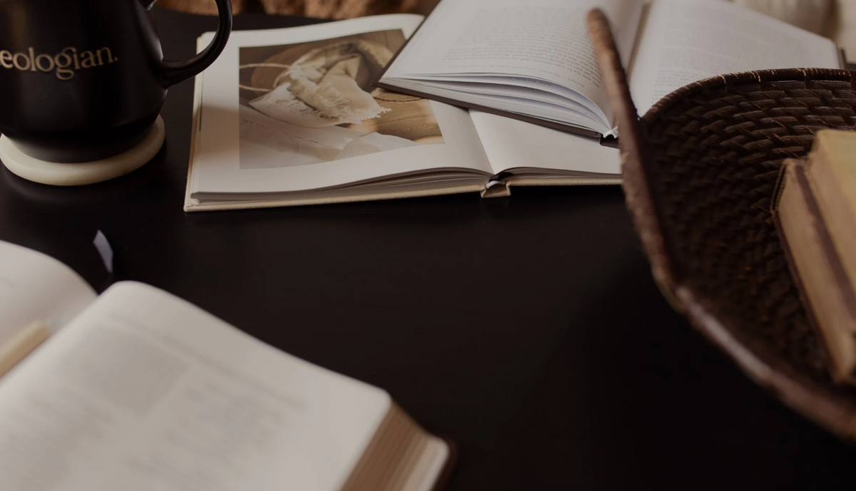 An open book on a dark colored table near a wicker basket and a coffee cup