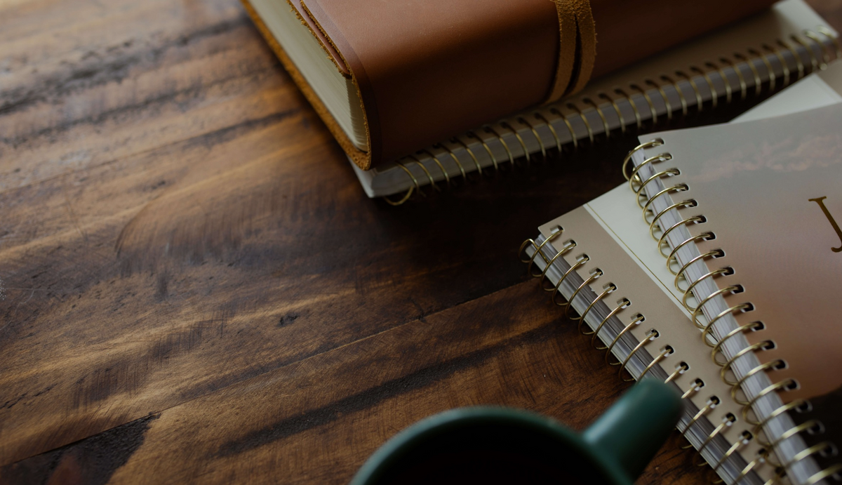 Two studies stacked near a bible on a wooden table near a coffee cup