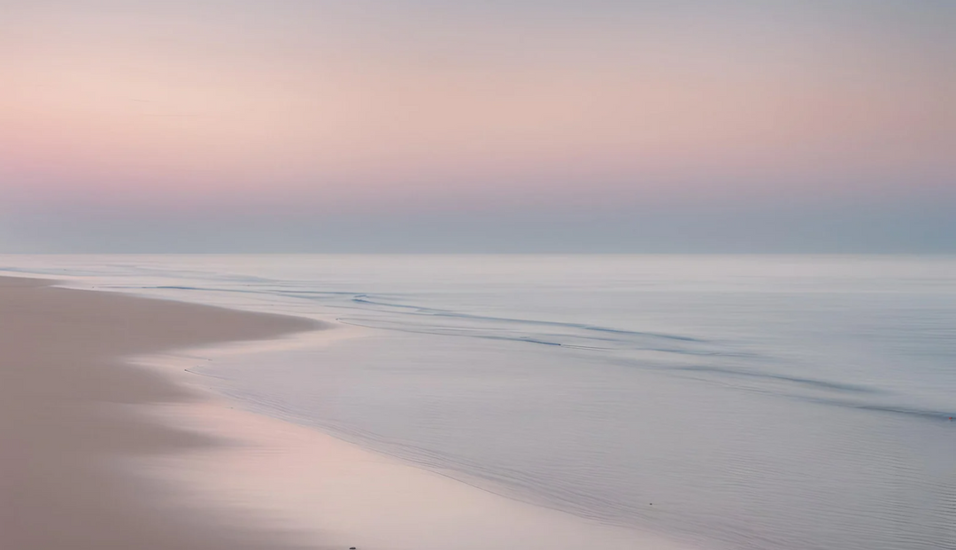 A clear ocean on the beachside with a clear pink and blue sky line
