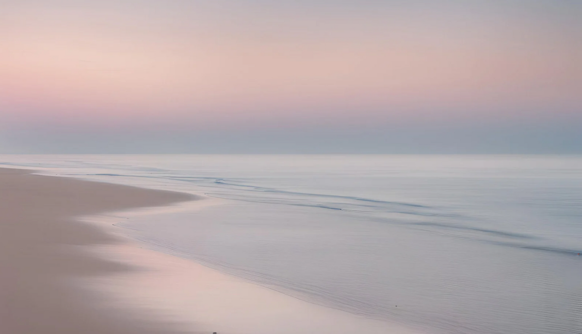 A clear ocean on the beachside with a clear pink and blue sky line