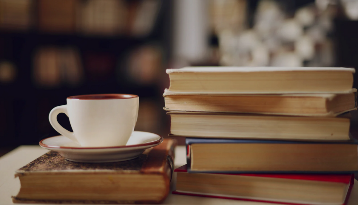A stack of books next to a cup on a saucer