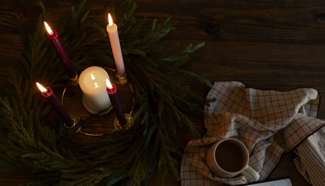 4 lit candles in the center of the wreath near a towel on a wooden table