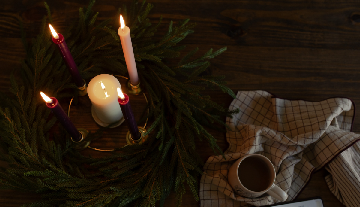 4 lit candles in the center of the wreath near a towel on a wooden table
