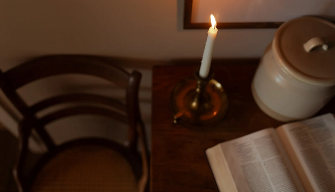 A lit candle on a candle lamp on a wooden table next to a chair