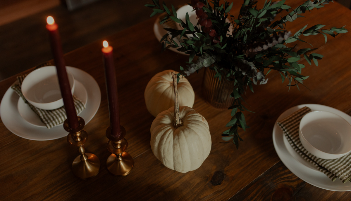 Two decorational pumpkins on a wooden table near lit candles and some greenery