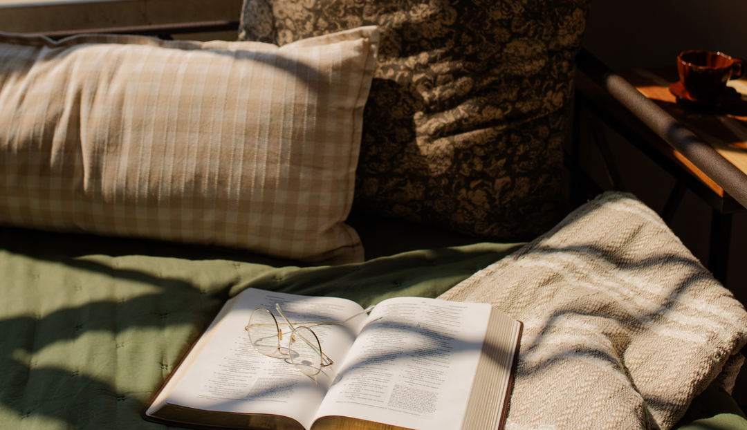 An open bible on a green blanket near some random pillows
