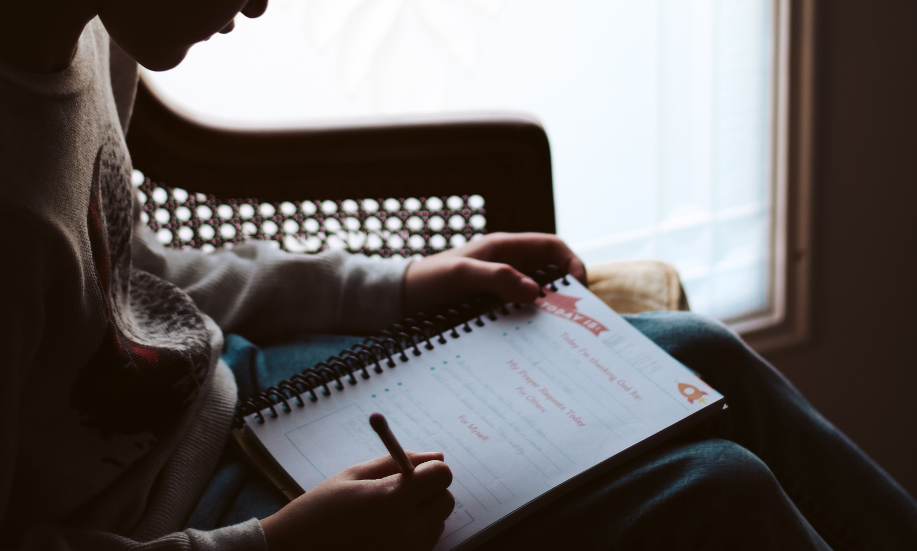 A person writing in a journal next to a window