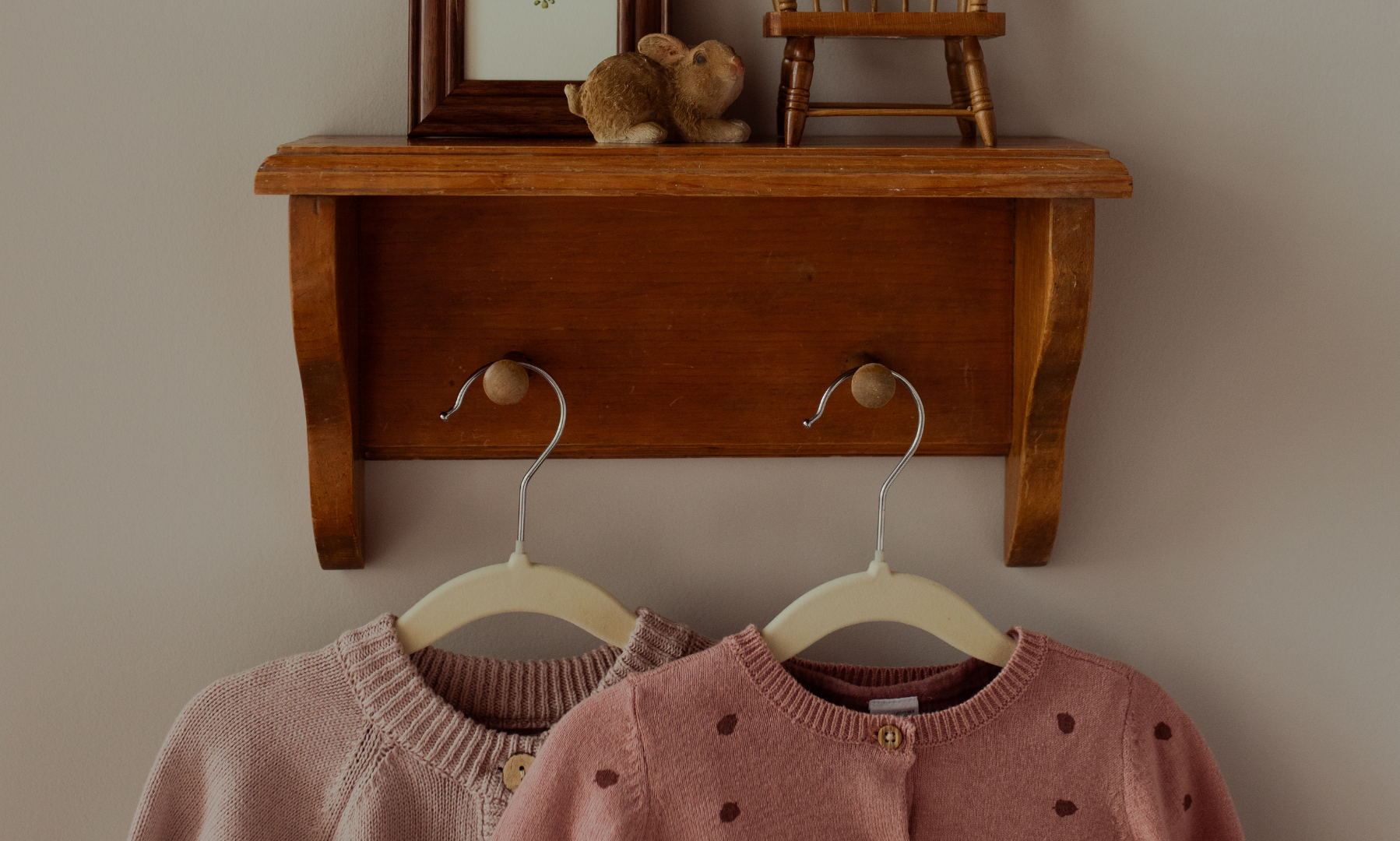 Two sweaters hanging on a shelf with some small items above it